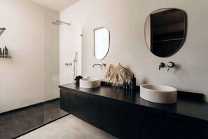 A modern bathroom with two sinks, a shower, and a large mirror.