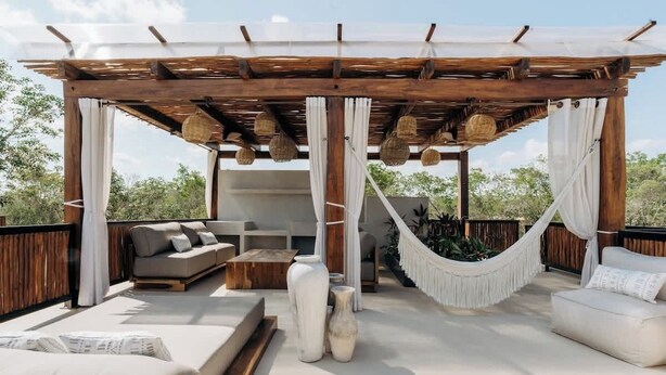 A covered outdoor seating area with a wooden pergola, cushioned seating, and hanging lights. - Casa Mazuri Jungle Villa Beach Club Access (Tulum)