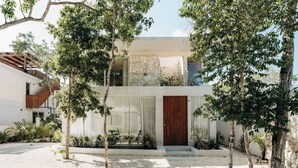 A modern building with a stone facade, a wooden door, and a well-maintained garden with trees and plants. - Casa Mazuri Jungle Villa Beach Club Access (Tulum)