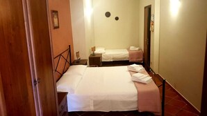 Habitación de hotel con dos camas, un armario de madera, una mesita de noche pequeña y una lámpara fijada a la pared.
