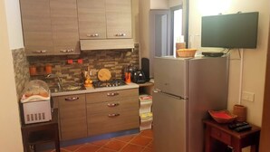 Una cocina compacta con armarios de madera, horno integrado, refrigerador y una pequeña mesa de madera con una cesta.
