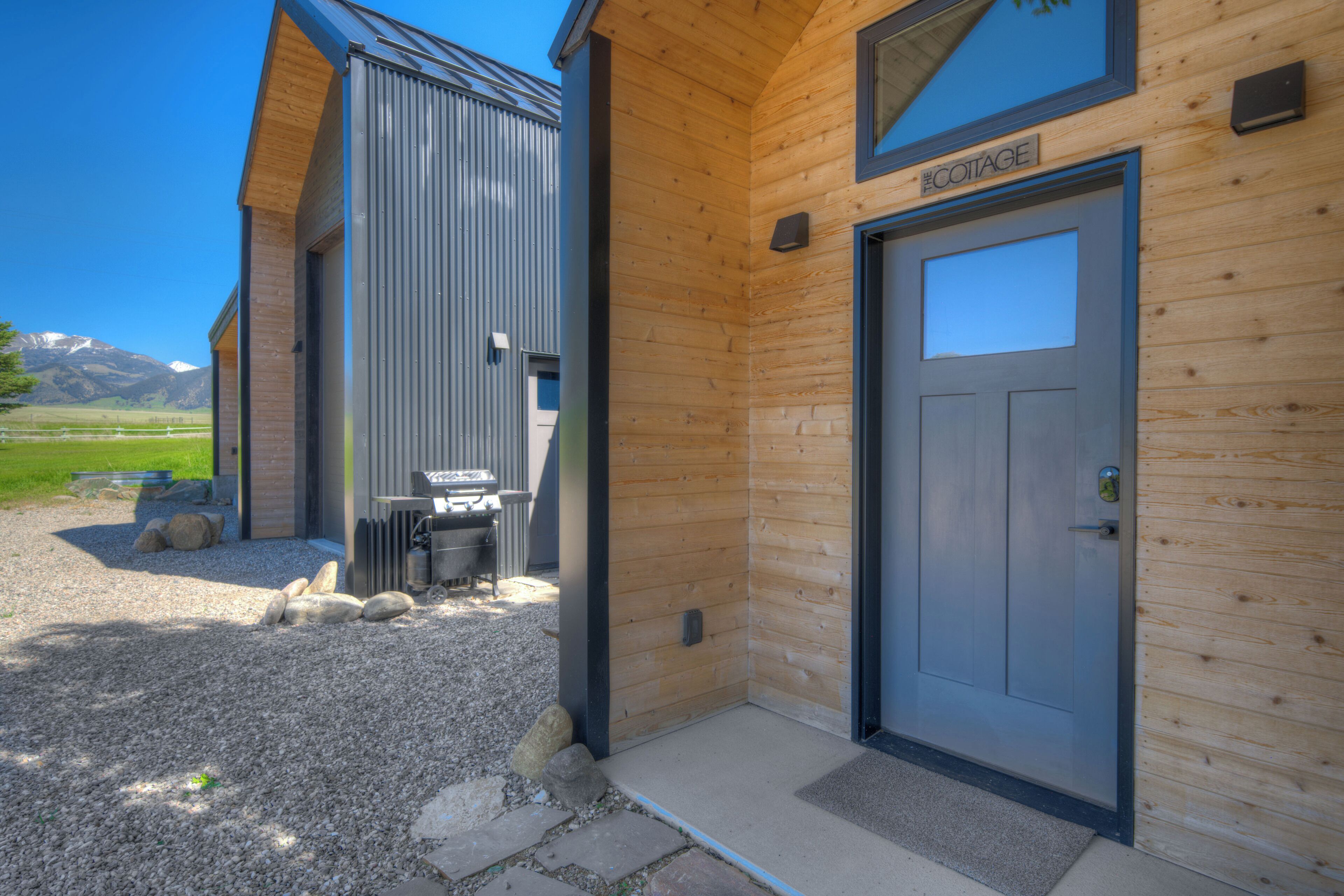 Een houten gebouw met een deur waarop 'COTTAGE' staat en een klein buitenterrein met een tafel en stoelen.
