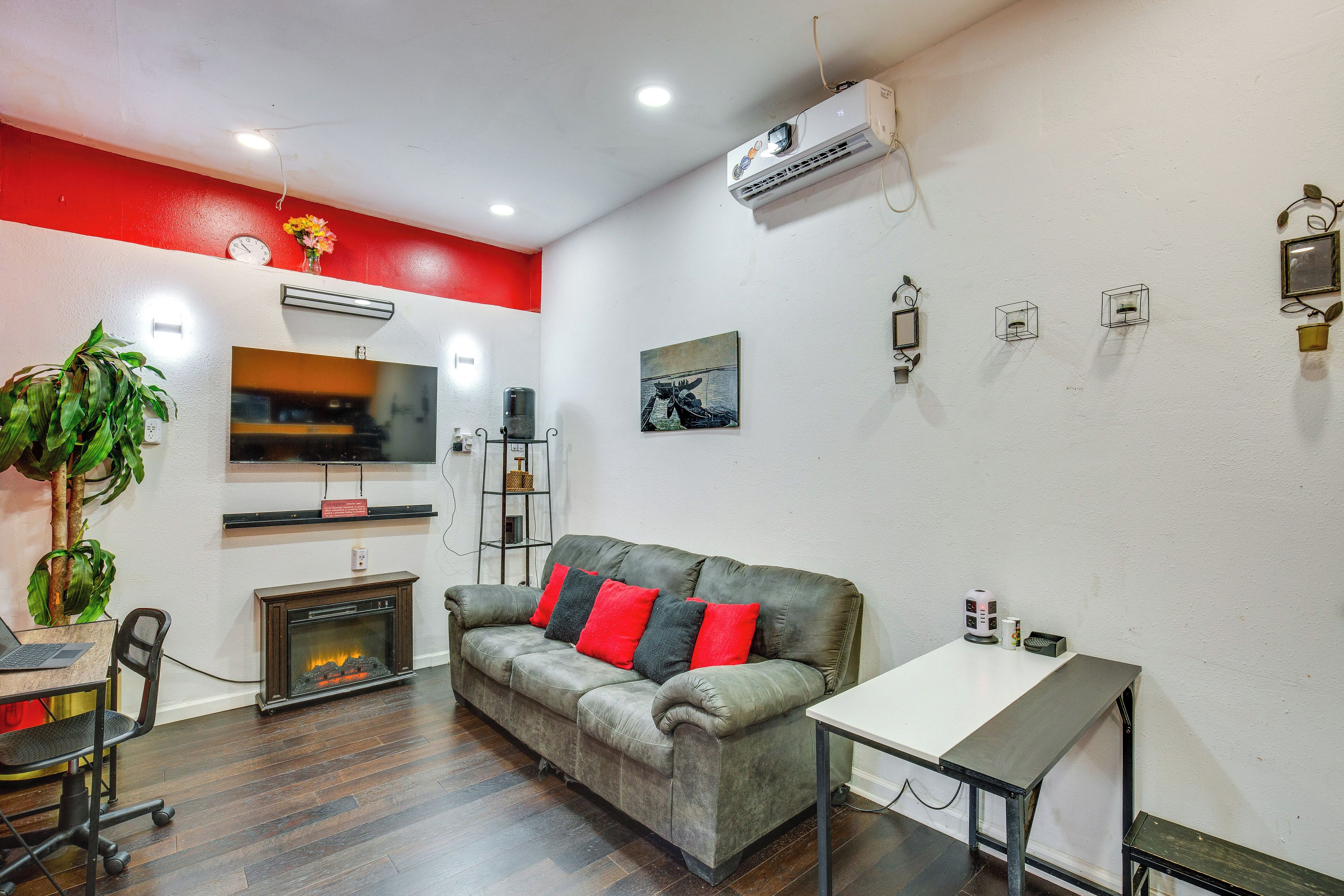 A modern living room with a fireplace, a sofa with red cushions, a dining table, and a TV mounted on the wall.