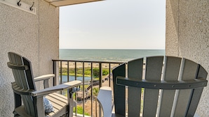 Ein Balkon mit zwei Adirondack-Stühlen, einem kleinen Tisch und Blick aufs Meer.
