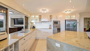 A modern kitchen with a large island, built-in appliances, and a large window. - The Dreamscape: Sea View Serenity on the Esplanade (Cairns)