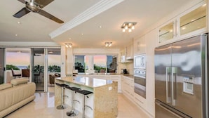 A modern kitchen with a large island, stainless steel appliances, and a ceiling fan. - The Dreamscape: Sea View Serenity on the Esplanade (Cairns)