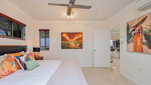A hotel room with a bed, ceiling fan, artwork, and a door leading to a bathroom. - The Dreamscape: Sea View Serenity on the Esplanade (Cairns)