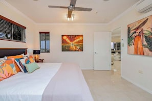 A hotel room with a bed, ceiling fan, artwork, and a door leading to a bathroom.