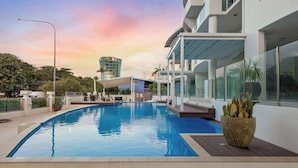 A modern hotel with a swimming pool, outdoor seating, and a view of a cityscape. - The Dreamscape: Sea View Serenity on the Esplanade (Cairns)