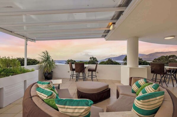 A covered outdoor seating area with a view of the ocean and mountains.