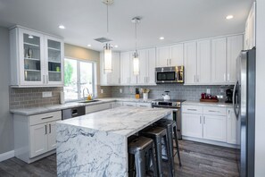 A modern kitchen with white cabinets, a marble island, stainless steel appliances, and pendant lighting. - 3BR - Poinsettia Pool Paradise! (Scottsdale)