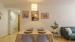 Ein Essbereich mit einem Tisch für vier Personen, zwei Stühlen, einer Hängelampe und drei gerahmten Kunstwerken an der Wand.