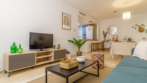 Ein Wohnzimmer mit Fernseher, einer Couch, einem Couchtisch und einem Essbereich mit Tisch und Stühlen.