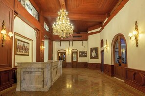 Un hall d’entrée spacieux avec un comptoir de réception en marbre, des panneaux de bois, un grand lustre et des luminaires fixés au mur.