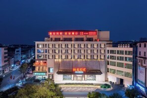 Ein mehrstöckiges Hotel mit markanter Eingangspartie, Parkplatz und Blick auf die Straße.