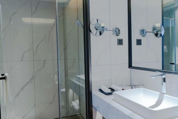 Ein modernes Badezimmer mit einer gläsernen Duschkabine, einem weißen Waschbecken und einem großen Spiegel.