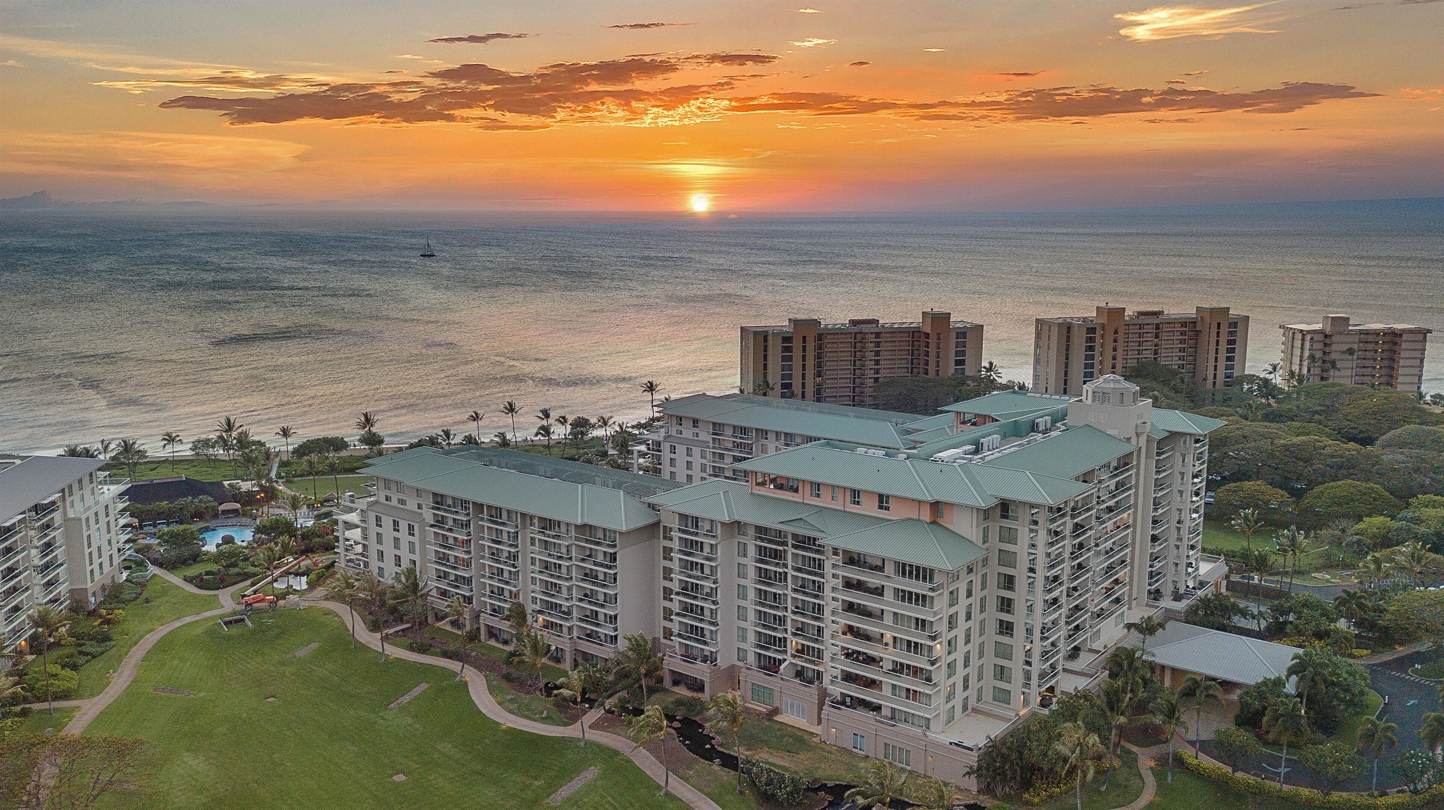 A high-rise hotel with multiple floors, a swimming pool, and a view of the ocean at sunset.