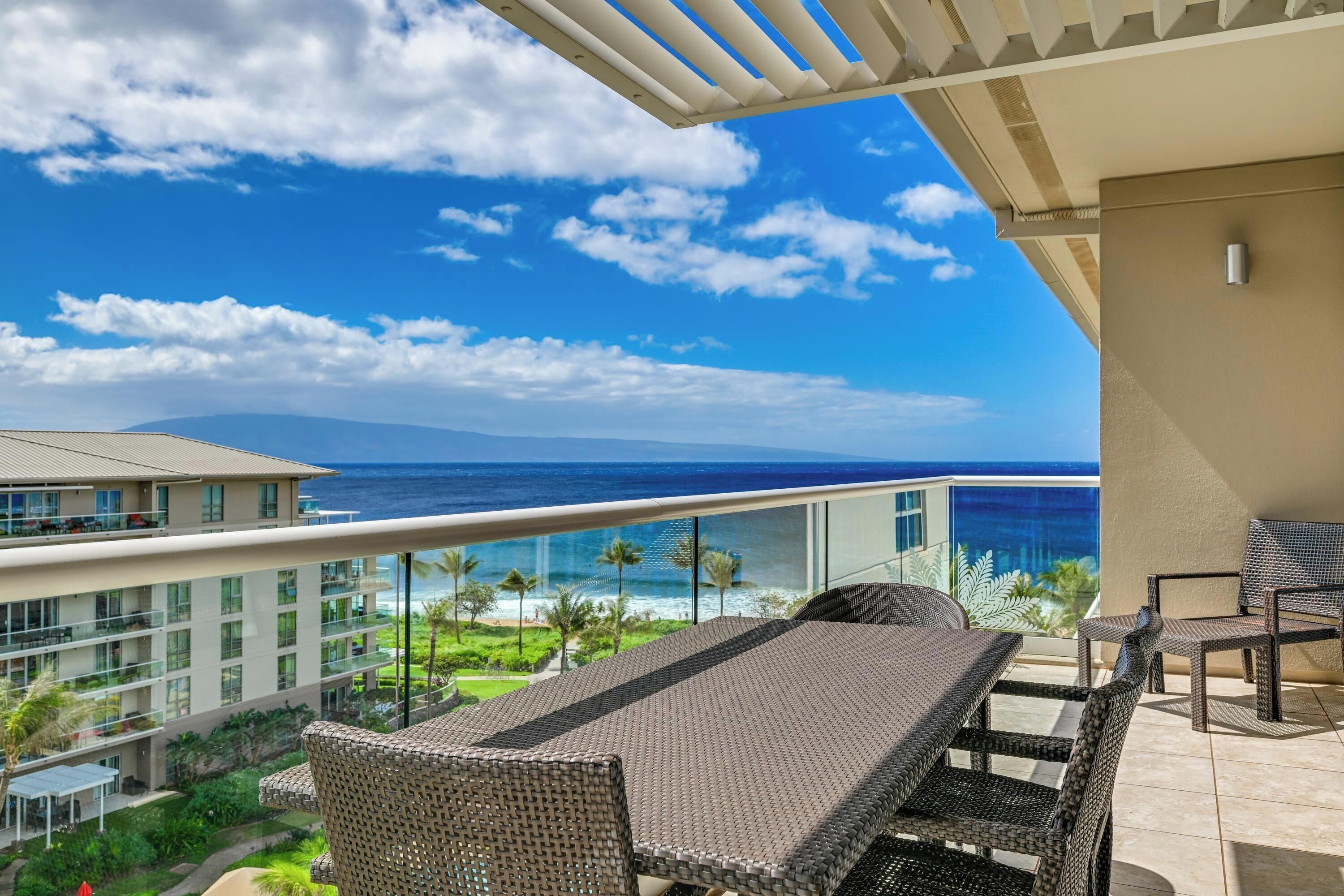 A balcony with wicker furniture overlooking a beach and ocean.