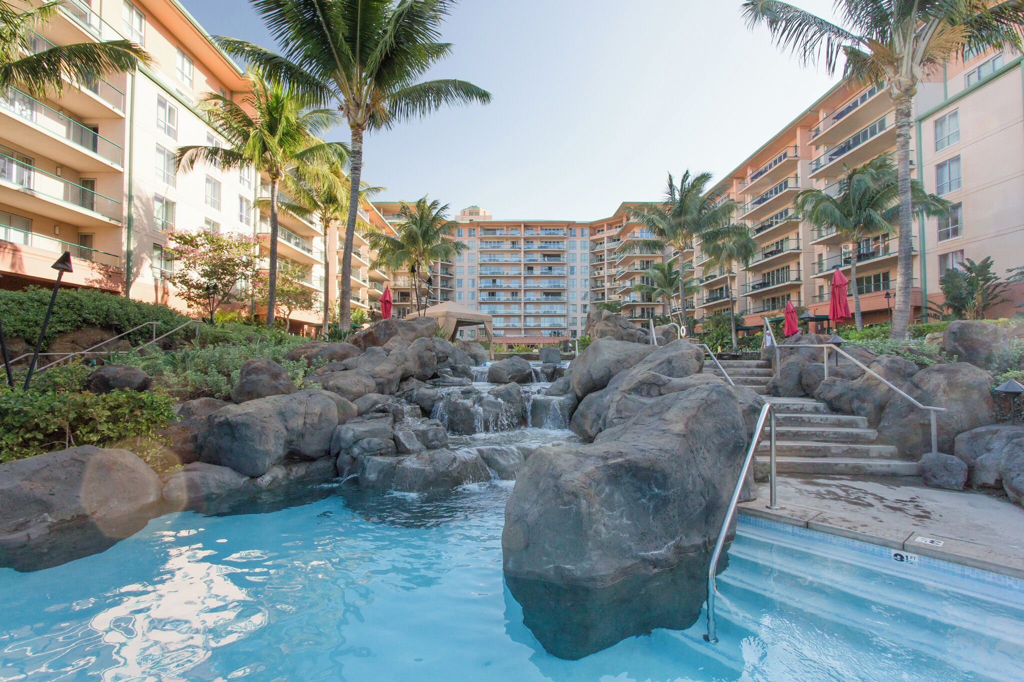 A resort pool with a waterfall, surrounded by palm trees and large rocks.