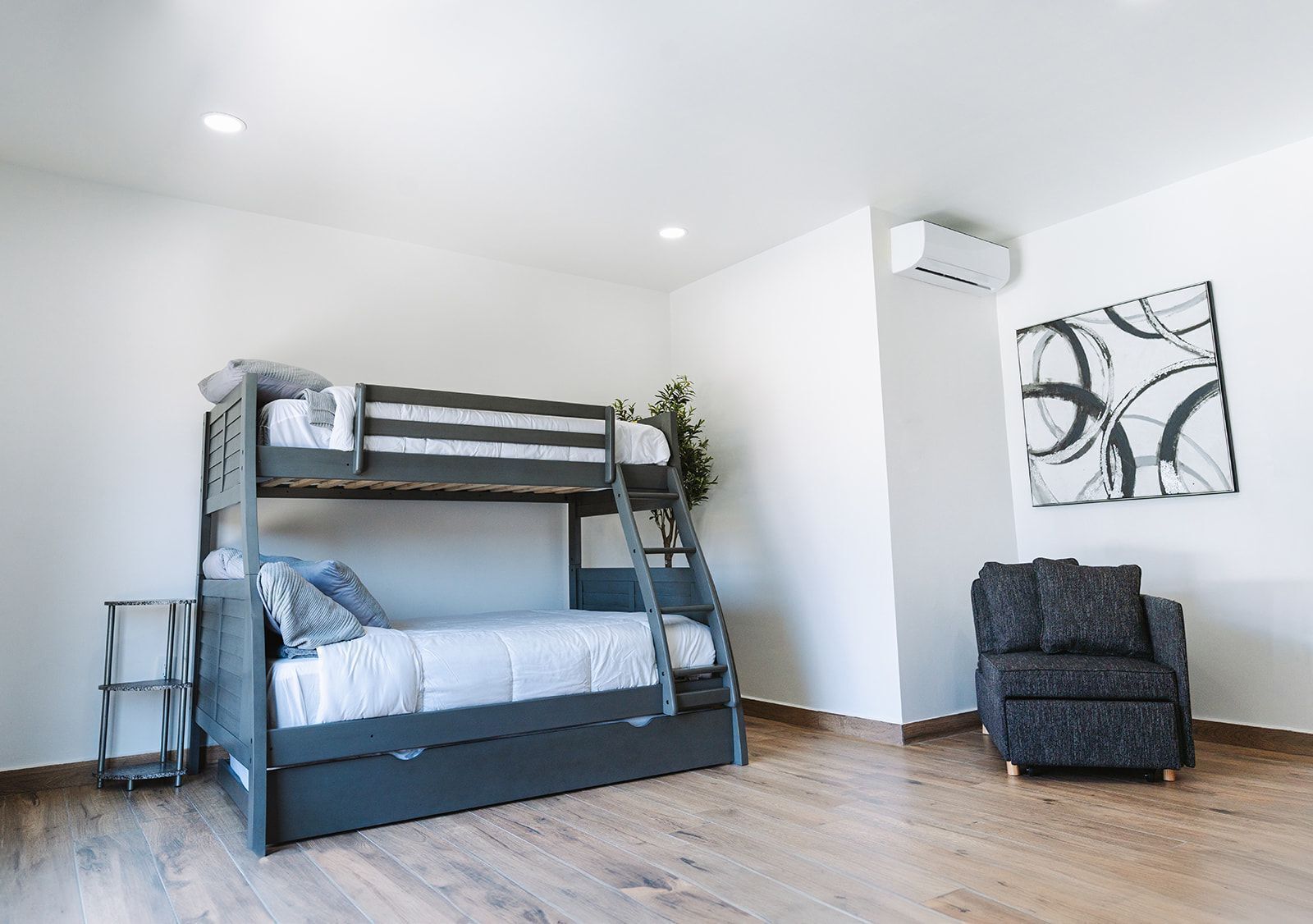 Dormitorio con literas, una mesita y un sillón gris.