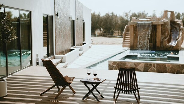 A modern outdoor seating area with two lounge chairs and a small table, overlooking a pool and a waterfall feature. - Casa Samaria (Valle de Guadalupe)