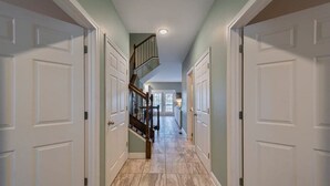 A hallway with white doors, a wooden staircase, and a tiled floor.