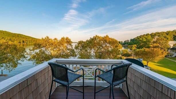 A balcony with two chairs overlooking a lake and trees.