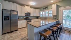 A modern kitchen with white cabinets, stainless steel appliances, a granite countertop island with bar stools, and a window with a view.