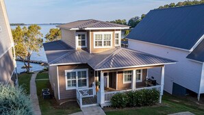 A two-story house with a covered porch, a small deck, and a view of the water.
