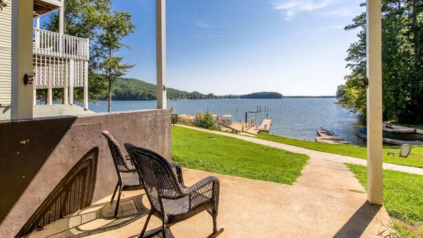 Une terrasse couverte avec des sièges d’extérieur, une vue sur un lac et un quai avec des bateaux.