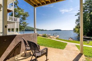 A covered patio with outdoor seating, a view of a lake, and a dock with boats.