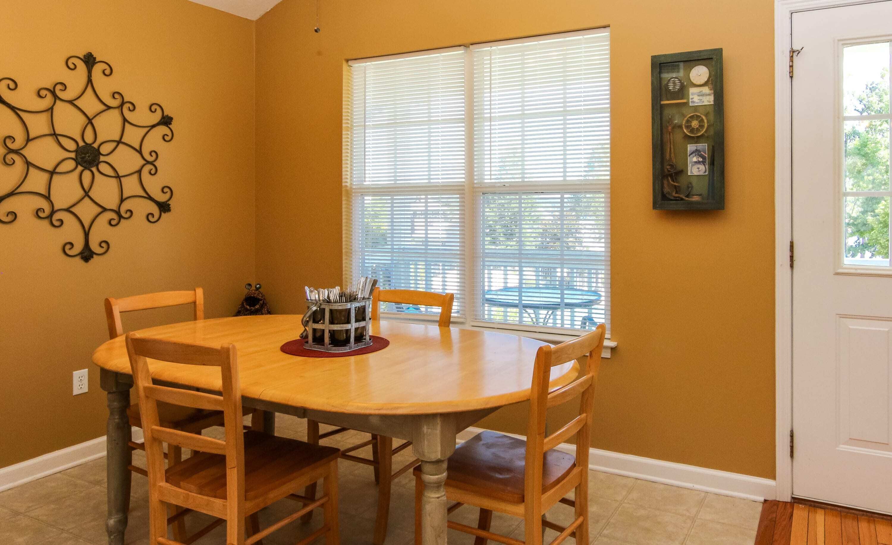 A dining area with a round wooden table, four wooden chairs, a metal utensil holder, and a decorative wall piece.