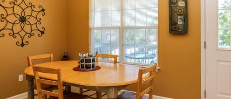 A dining area with a round wooden table, four wooden chairs, a metal utensil holder, and a decorative wall piece.