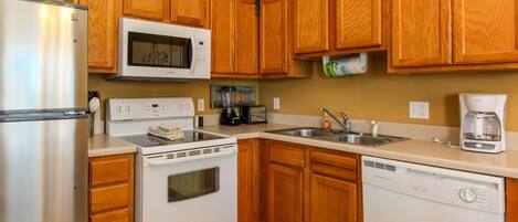 A kitchen with wooden cabinets, a stainless steel refrigerator, a microwave, an oven, a dishwasher, and a coffee maker.