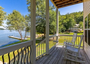 Een houten terras met een balustrade, met uitzicht op een meer en een huis.