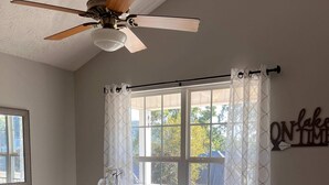 Ein Essbereich mit einem runden Tisch, vier Stühlen, einem Deckenventilator und einem Fenster mit Vorhängen.
