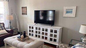 Ein Wohnzimmer mit Fernseher auf einem weißen Schrank, einer Bank mit Tablett und einem Sofa.