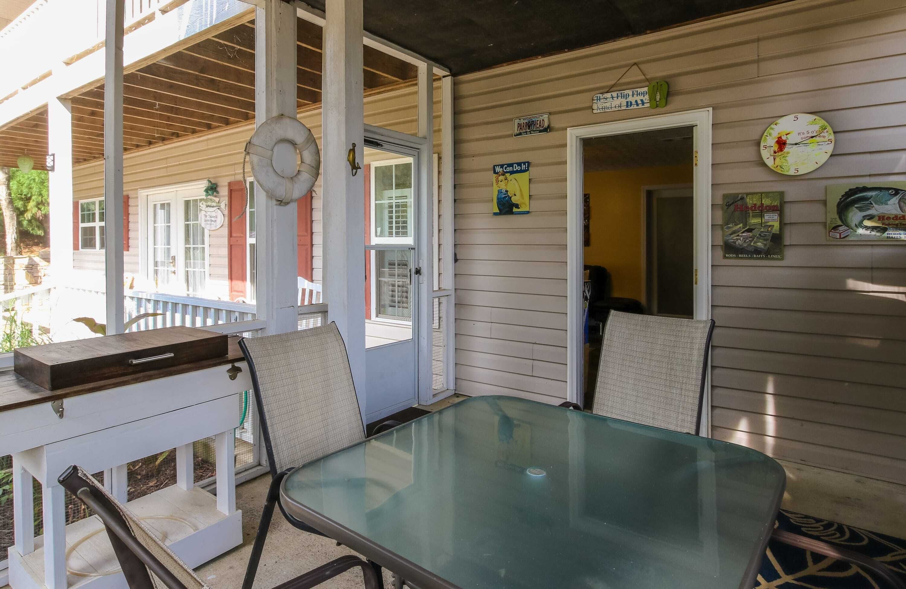 A covered patio area with a glass table and chairs, a wooden bench, and a door leading to a room.