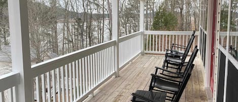 A covered outdoor area with a wooden deck, white railings, and a row of black chairs.