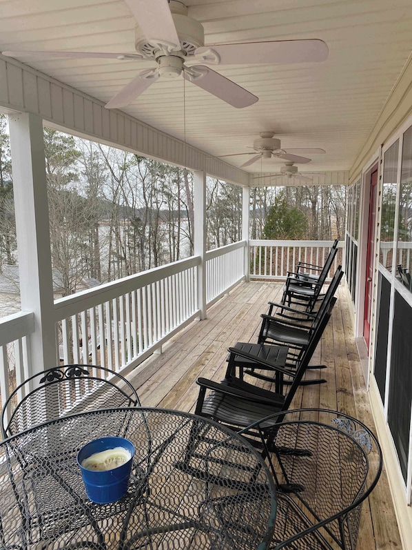 A covered outdoor area with a wooden deck, white railings, and a row of black chairs.