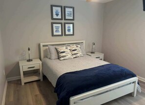 A bedroom with a bed, two bedside tables, a nightstand, a headboard, and four framed pictures on the wall. - House # 29 -Castaway (Pet Friendly) (Leesburg)