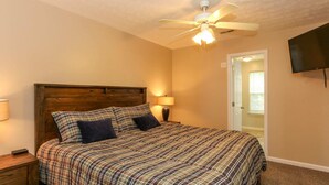 A bedroom with a wooden headboard, a bed with plaid bedding, a ceiling fan, a bedside lamp, and a TV mounted on the wall. - House# 30 Endless View Not Pet-Friendly (Leesburg)