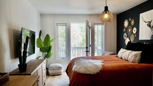 Une chambre à coucher comprenant un lit, une commode en bois, une plante en pot, un téléviseur et un mur décoré d’assiettes.