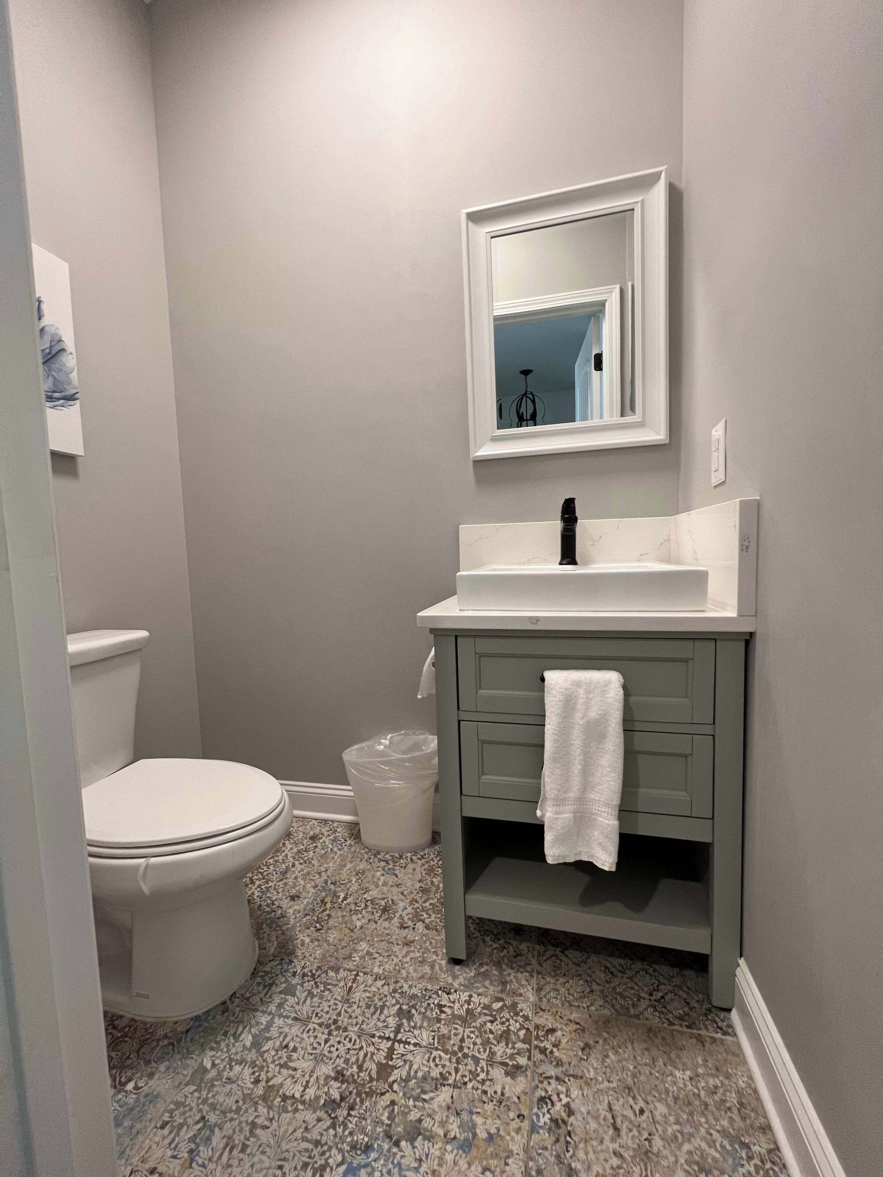 A bathroom with a toilet, a sink with a mirror, and a patterned floor.