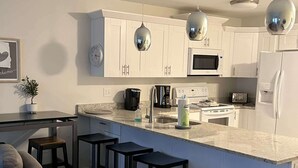 Una cocina moderna con armarios blancos, una isla central con taburetes e iluminación colgante.