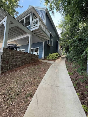 A two-story house with a covered porch, a stone retaining wall, and a concrete pathway.