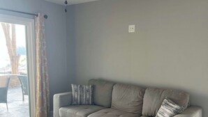 Una sala de estar con un sofá modular, un ventilador de techo y vistas a un espacio exterior a través de un ventanal.
