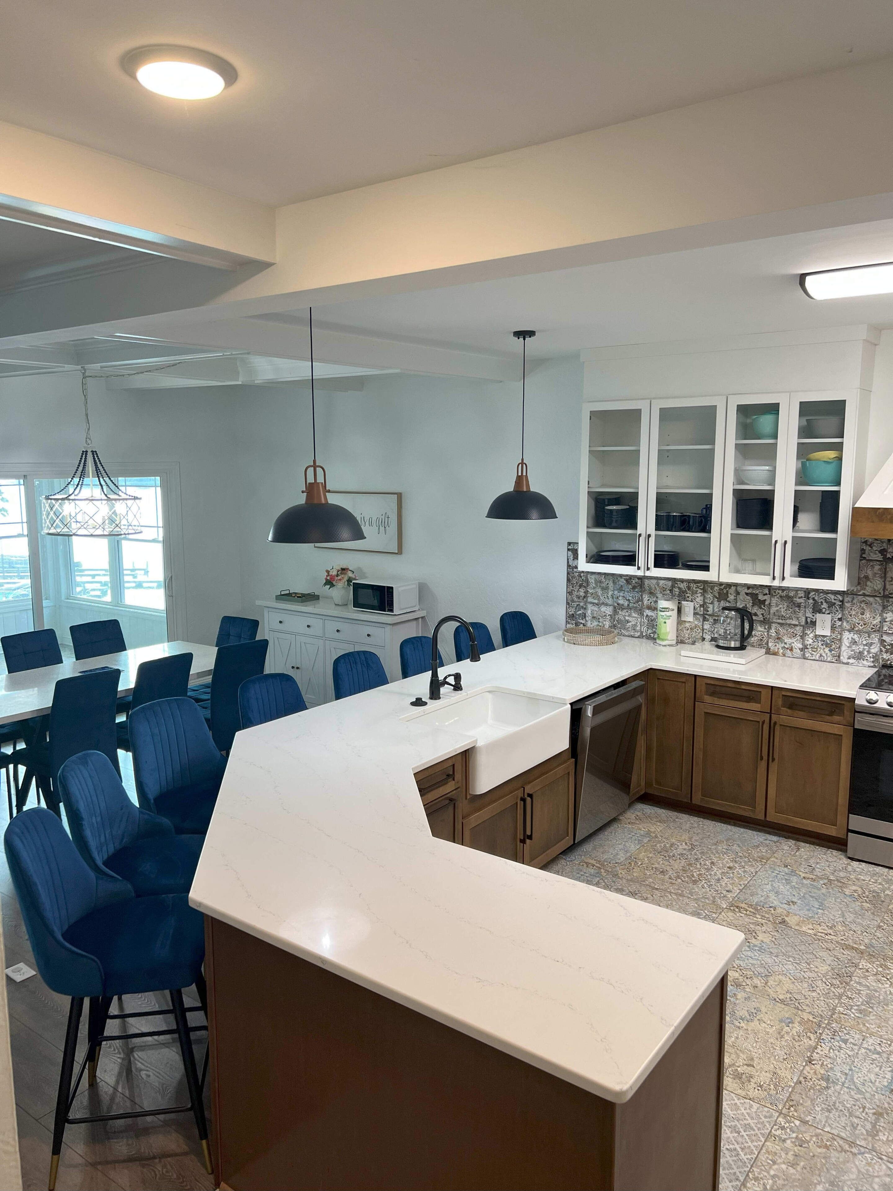 A modern kitchen with white cabinetry, a marble countertop, and blue chairs around a dining table.