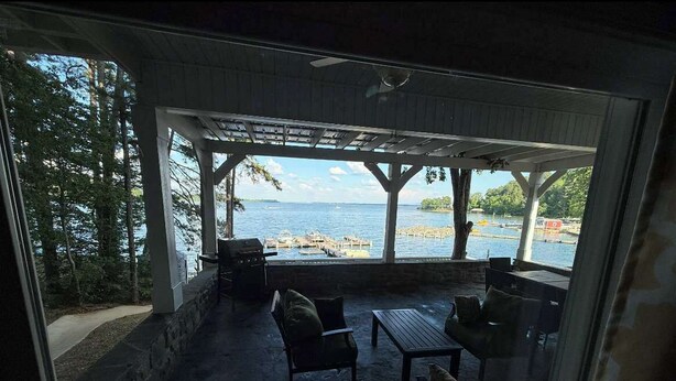 Un patio exterior con vistas a una masa de agua, mobiliario de madera y una estructura de pérgola.