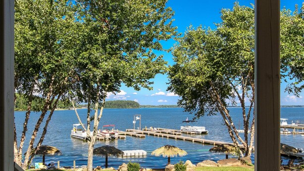 Une vue sur le lac, avec un quai, des bateaux et une zone herbeuse bordée d’arbres.